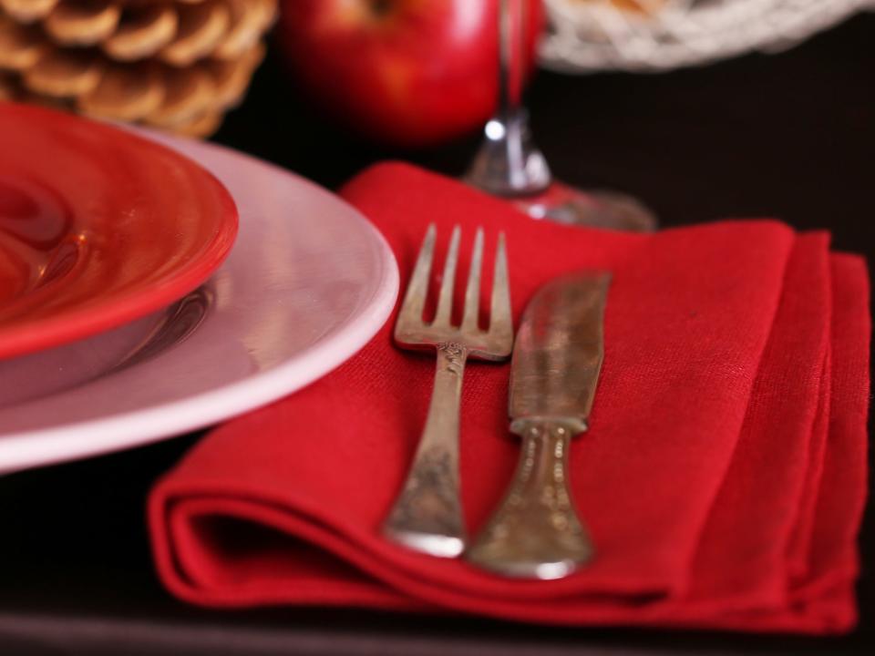 Cranberry napkins next to red plate in front of basket of apples on table