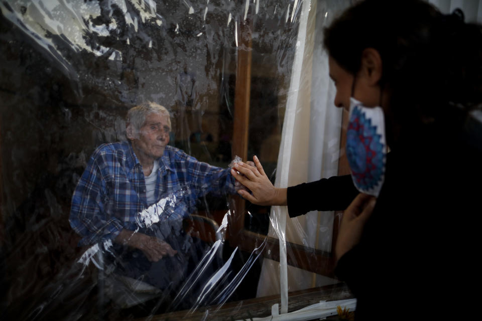 Victor Tripiana, 86, reaches out to touch the hand of his daughter-in-law Silvia Fernandez Sotto, separated by a plastic sheet to prevent the spread of COVID- 19 at the Reminiscencias residence for the elderly in Tandil, Argentina, Sunday, April 4, 2021. Residents here do not have physical contact with their families or leave the residence due to the pandemic, but stay active with group activities within the facility. (AP Photo/Natacha Pisarenko)
