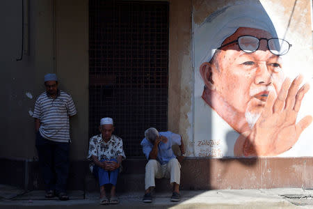 People sit next to a mural of the late former Party Islam Se-Malaysia (PAS) president, Tuan Guru Nik Abdul Nik Mat at Medan Ilmu in Kota Bharu, Kelantan, Malaysia April 13, 2018. REUTERS/Stringer