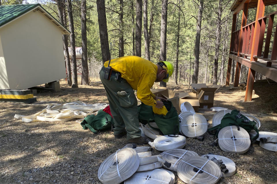 In this photo released by the U.S. Forest Service, a firefighter gathers hose and fittings to assemble sprinkler protection systems in the Santa Fe National Forest in New Mexico on Thursday, April 28, 2022. Thousands of firefighters continued to slow the advance of destructive wildfires in the Southwestern U.S., but officials warned they were bracing for the return Friday of the same dangerous conditions that quickly spread the wind-fueled blazes a week ago. (J. Michael Johnson/U.S. Forest Service via AP)