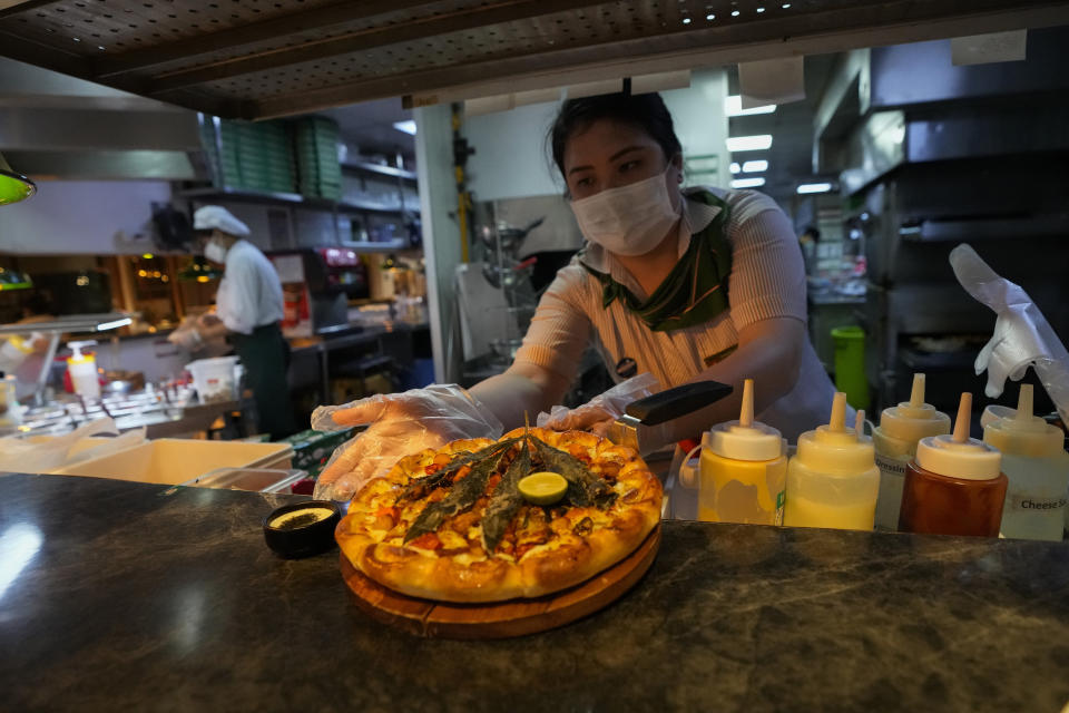 A staff member prepares to serve a pizza topped with a cannabis leaf to the customers at a restaurant in Bangkok, Thailand on Nov. 24, 2021. The Pizza Company, a Thai major fast food chain, has been promoting its "Crazy Happy Pizza" this month, an under-the-radar product topped with a cannabis leaf. It’s legal but won’t get you high. (AP Photo/Sakchai Lalit)