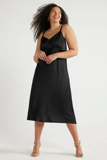 model in a black midi slip dress and strappy sandals, posing with a smile. Ideal for a semi-formal event