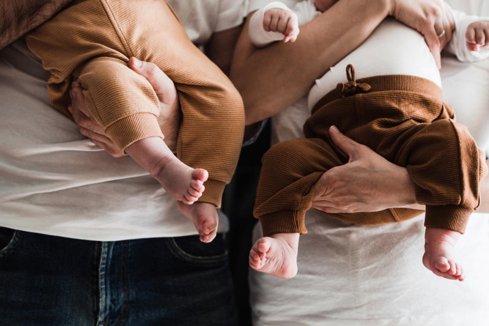 Two adults holding two babies, each wearing similar ribbed pants. Faces are not visible