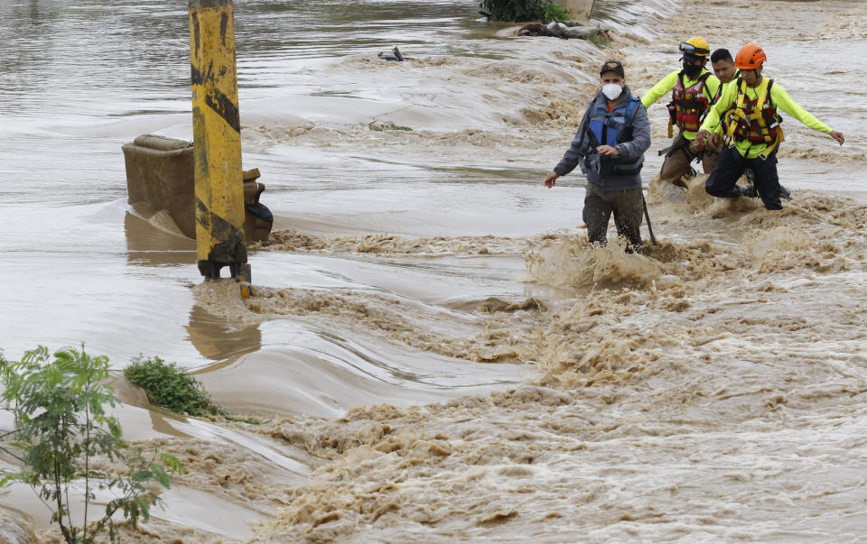 Rescuers wade through a flooded road after the passing of Hurricane Iota in La Lima, Honduras, Wednesday, Nov. 18, 2020. Iota flooded stretches of Honduras still underwater from Hurricane Eta, after it hit Nicaragua Monday evening as a Category 4 hurricane and weakened as it moved across Central America, dissipating over El Salvador early Wednesday. (AP Photo/Delmer Martinez)
