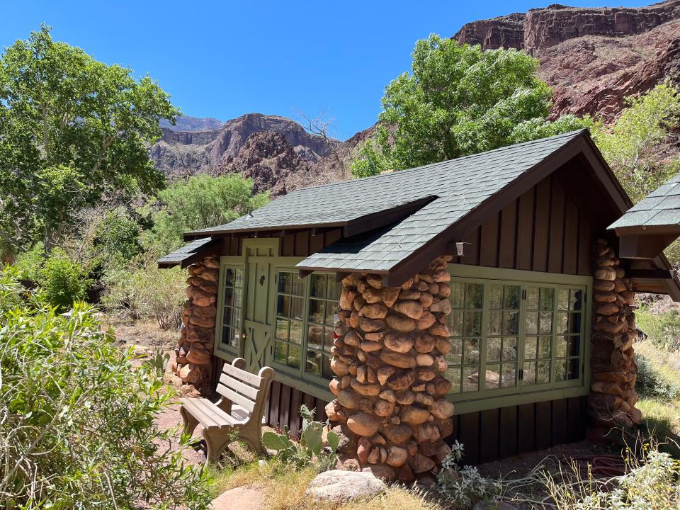 A stone and log cabin next to trees and mountains.