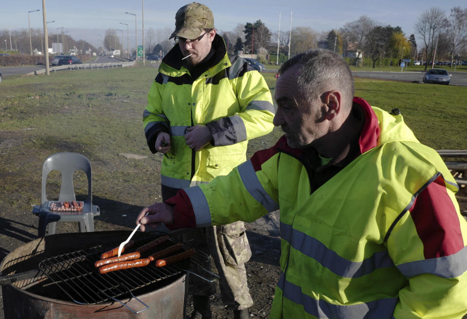 Demonstrators wearing their yellow vests prepare sausages for lunch on a traffic circle, Tuesday, Dec. 11, 2018 in Douai, northern France. President Emmanuel Macron broke his silence Monday on the exceptional protests shaking France and his presidency, promising broad tax relief for struggling workers and pensioners — and acknowledging his own responsibility in fueling the nation's anger. (AP Photo/Michel Spingler)