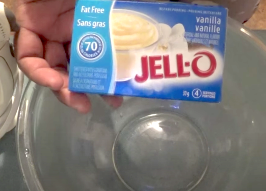 holding up a container of jello-instant vanilla pudding mix over a mixing bowl