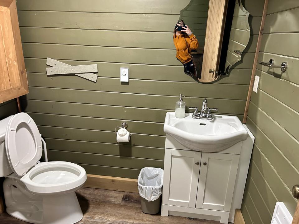 green wood panel bathroom with white sink and toilet and mirror above sink in lost Boys Treehous