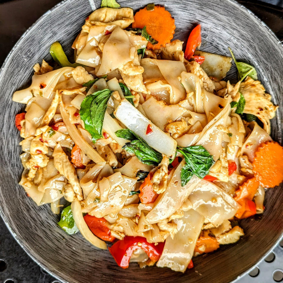 A plate of stir-fried noodles with chicken and various vegetables, garnished with basil