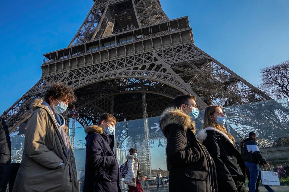 People wearing face masks to protect against COVID-19 walk past the Eiffel Tower in Paris, Tuesday, Dec. 21, 2021.