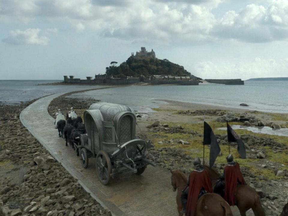 A scene from "House of the Dragon," showing a castle on an island of land in the middle of an ocean bay.