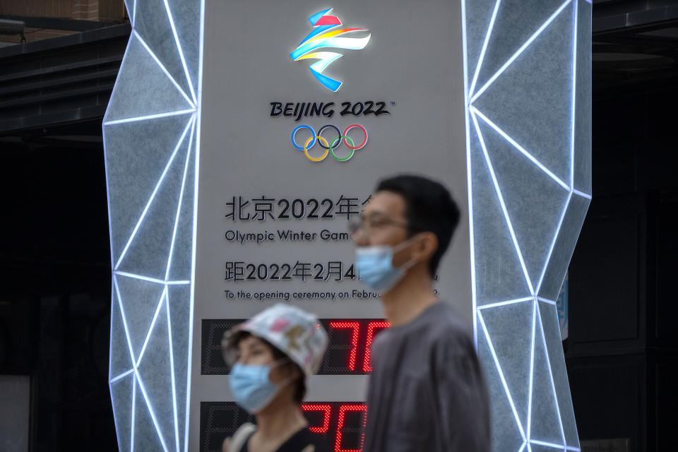 People wearing face masks to protect against COVID-19 walk past a display showing a countdown clock to the 2022 Winter Olympics in Beijing, Wednesday, Aug. 18, 2021. Beijing's top official is reiterating the need for strict anti-coronavirus measures at next year's Winter Olympics, now less than 200 days away, although it remains unclear whether spectators will be permitted. (AP Photo/Mark Schiefelbein)