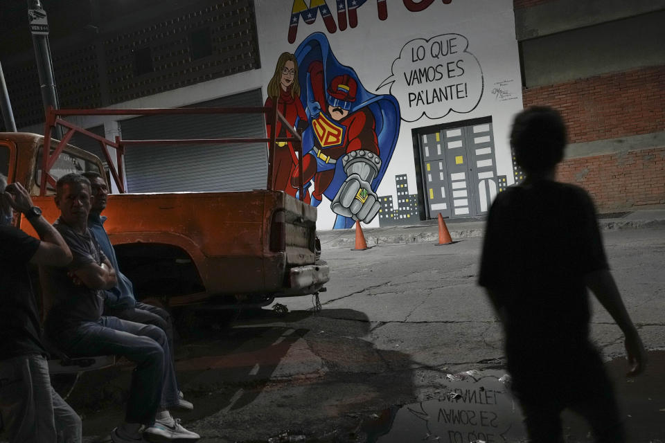 FILE - People stand near a mural of a cartoon character known as "Super Bigote", or "Super Moustache", that casts Venezuela's President Nicolas Maduro as a super hero in Caracas, Venezuela, March 3, 2023. The United Socialist Party of Venezuela has controlled the nation and its oil wealth for a quarter-century, 15 years under Hugo Chávez and a decade under Maduro. (AP Photo/Matias Delacroix, File)