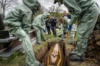 In this photo taken on Saturday, May 2, 2020, funeral workers, wearing protective suits, lower the coffin of Semen Muchka, 71, who died of coronavirus disease, into the grave at a cemetery in Krynytsya, Ukraine. Ukraine's troubled health care system has been overwhelmed by COVID-19, even though it has reported a relatively low number of cases. (AP Photo/Evgeniy Maloletka)