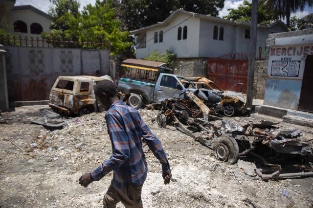 A man walks past charred and abandoned vehicles in La Plaine neighborhood of Port-au-Prince, Haiti, Friday, May 6, 2022. Fighting raged in four districts on the northern side of Port-au-Prince that has surged as increasingly powerful gangs try to control more territory during the political power vacuum left by the July 7 assassination of President Jovenel Moise. (AP Photo/Odelyn Joseph)