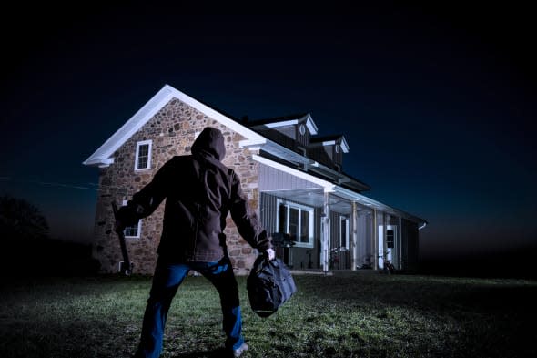 A photograph of a burglar outside a house at night.