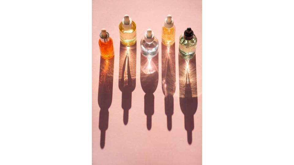 From above bottles with various moisturizing products arranged in line on pink background