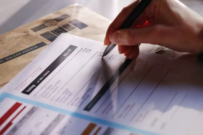 Stock image showing a woman’s hand filling in a postal ballot / voting form.