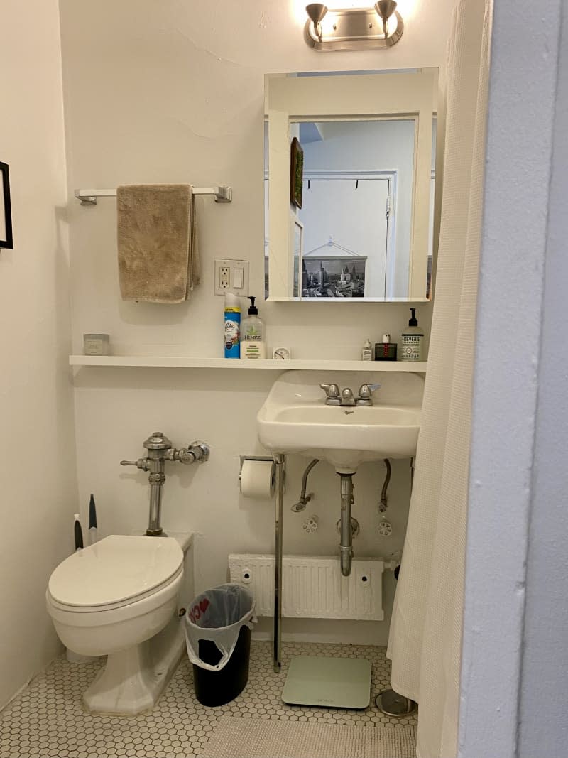 Bathroom with tile floor and exposed pipes leading to a shelf and rectangular mirror.