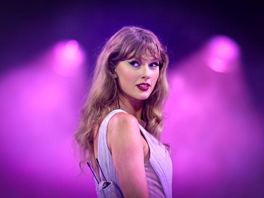 Swift at a stop on "The Eras Tour" in London, looking over her shoulder with purple smoky lighting in the background.