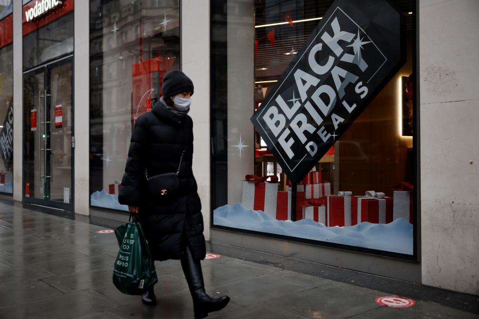 A woman walks in the rain past Black Friday offers in a shop in central London on November 20, 2020, as life under a second lockdown continues in England. (Photo by Tolga Akmen / AFP) 