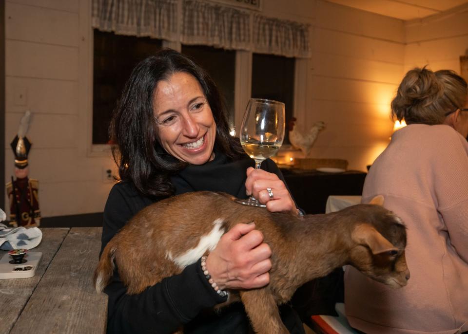 Laura Azevedo of Stratham enjoys a glass of wine while holding Kit, a baby goat, Wine-yasa Goat Yoga night at Legacy Lane Farm in Stratham.