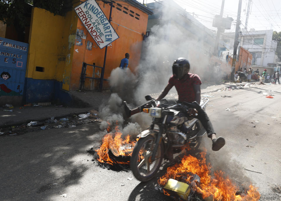 A man drives his motorcycle through a burning barricade during anti-government protests in Port-au-Prince, Haiti, Friday, Oct. 11, 2019. Protesters burned tires and spilled oil on streets in parts of Haiti's capital as they renewed their call for the resignation of President Jovenel Moïse just hours after a journalist was shot to death. (AP Photo/Rebecca Blackwell)