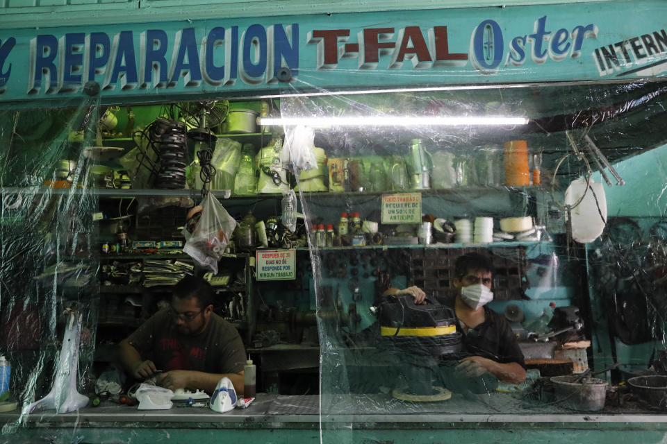 Workers in a small appliance repair shop work behind plastic sheeting to reduce the spread of coronavirus, in central Mexico City, Monday, July 6, 2020. After three months of shutdown, officials allowed a partial reopening of downtown last week, although COVID-19 cases continue to climb. (AP Photo/Rebecca Blackwell)