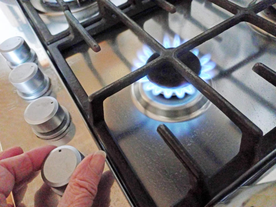 A hand turns the knob on a gas hob as blue flames come out of the stove