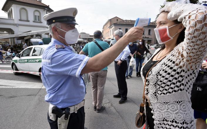A police officer checks the body temperature of a woman at a market in Treviglio, near Bergamo - Shutterstock