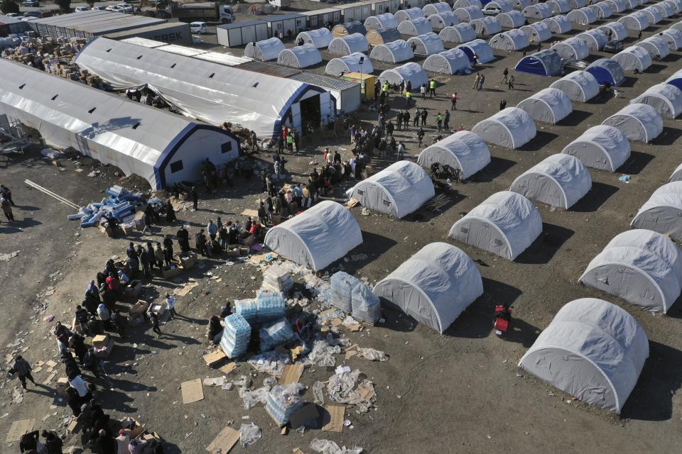 FILE - People who lost their houses in the devastating earthquake, lineup to receive aid supplies at a makeshift camp, in Iskenderun city, southern Turkey, on Feb. 14, 2023. Hundreds of thousands of people are seeking shelter after the Feb. 6 earthquake in southern Turkey left homes unlivable. Many survivors have been unable to find tents or containers dispatched to the region by the government and aid agencies, Instead they have sought refuge in any structure that can protect them from the winter conditions, including greenhouses, rail carriages and factories. (AP Photo/Hussein Malla)