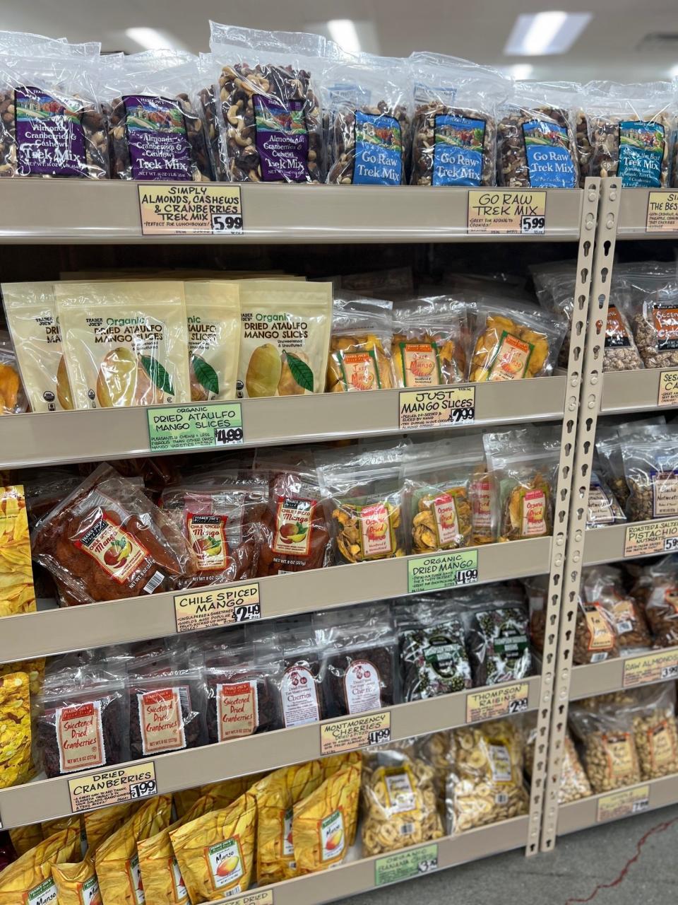 Grocery shelf stocked with various packaged nuts, dried fruits, and snack mixes, each with price labels