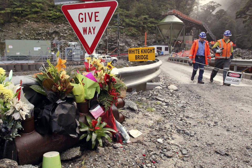 FILE - Workers walks past a bouquet of flowers for victims of mine explosion at the Pike River mine at Greymouth, New Zealand on June 28, 2011. More than a decade after a methane explosion killed 29 workers at the New Zealand coal mine, police said on Wednesday, Nov. 17, 2021, they have finally found at least two of the bodies thanks to new camera images. (Ian McGregor/Pool Photo via AP, File)