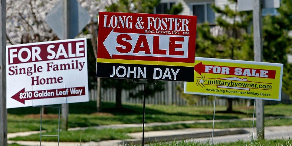 For sale signs stand on a medium strip in a housing development