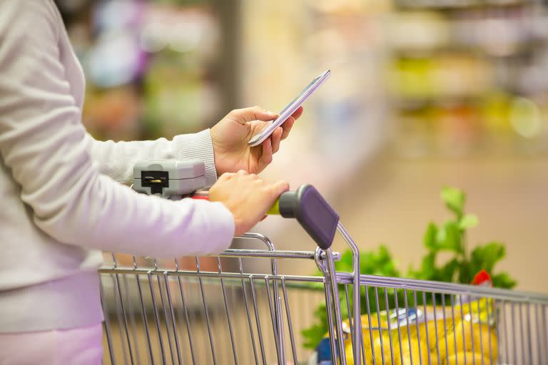 Woman using mobile phone while shopping in supermarket, trolley