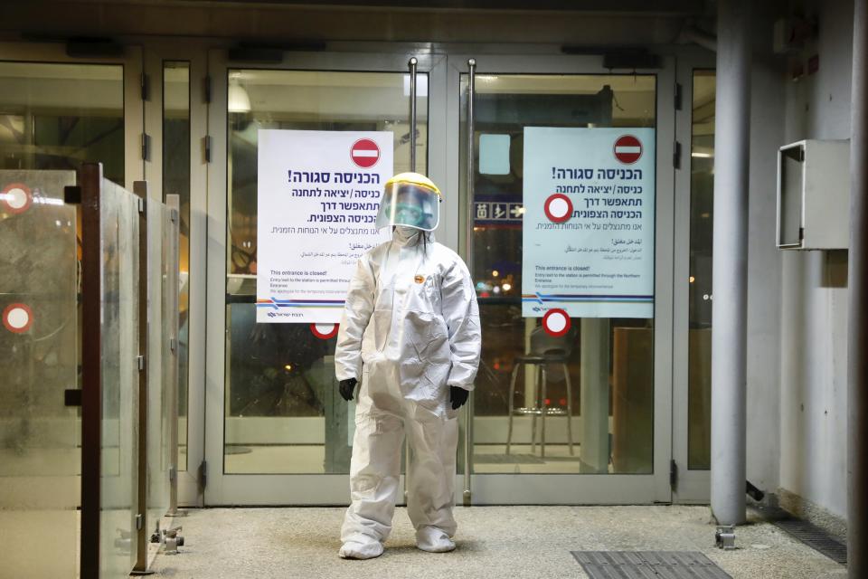 ‏A municipality worker blocks the door as a firefighter sprays disinfectant as a precaution‏ against the coronavirus at the Moshe Dayan Railway Station in Rishon LeTsiyon, Israel, Sunday, March 22, 2020. (AP Photo/Ariel Schalit)