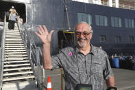 A passenger of the MS Westerdam, owned by Holland America Line, cheers after they disembark from the MS Westerdam, back, at the port of Sihanoukville, Cambodia, Saturday, Feb. 15, 2020. After being stranded at sea for two weeks because five ports refused to allow their cruise ship to dock, the passengers of the MS Westerdam were anything but sure their ordeal was finally over. (AP Photo/Heng Sinith)