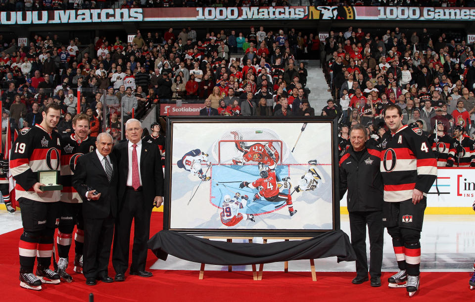 OTTAWA, CANADA - FEBRUARY 11: Chris Phillips #4 of the Ottawa Senators is presented with a painting and stands along with Jason Spezza #19, Daniel Alfredsson #11, Jim Gregory (3rdFL), Brian Murray (4thFL), general manager of the Ottawa Senators, Eugene Melnyk (2ndFR), owner, governor and chairman of the Ottawa Senators during a pre-game ceremony to honour Phillips having played 1000th career games prior to an NHL game against the Edmonton Oilers at Scotiabank Place on February 11, 2012 in Ottawa, Ontario, Canada. (Photo by Jana Chytilova/Freestyle Photography/Getty Images)