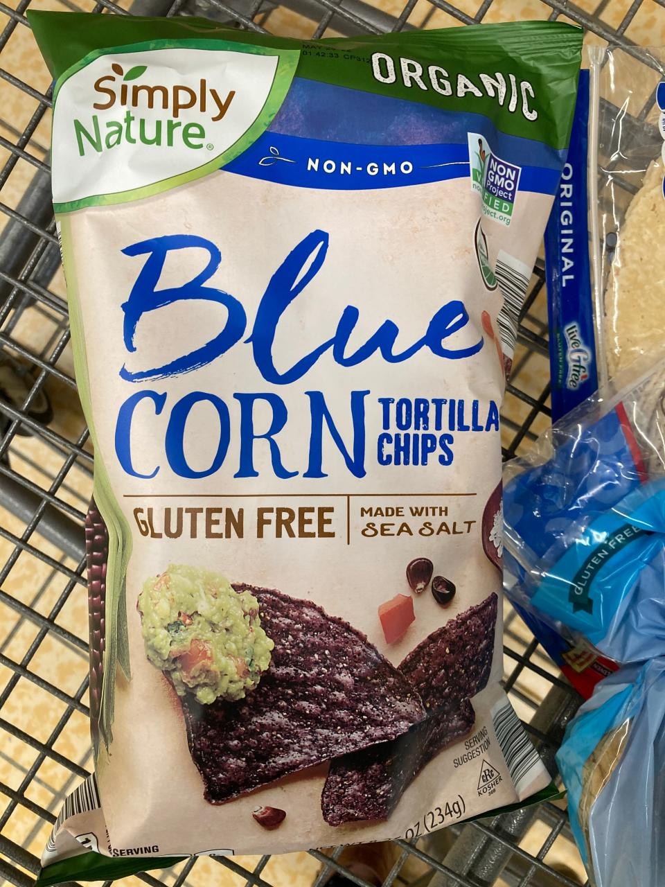 beige, blue, and green bag of Simply nature's blue corn tortilla chips in cart at Aldi