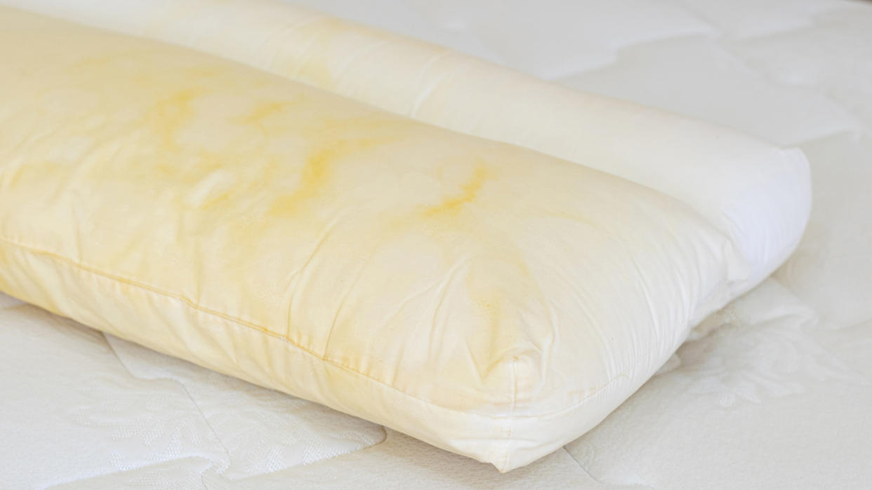  Image shows a white pillow and mattress covered in yellow stains. 