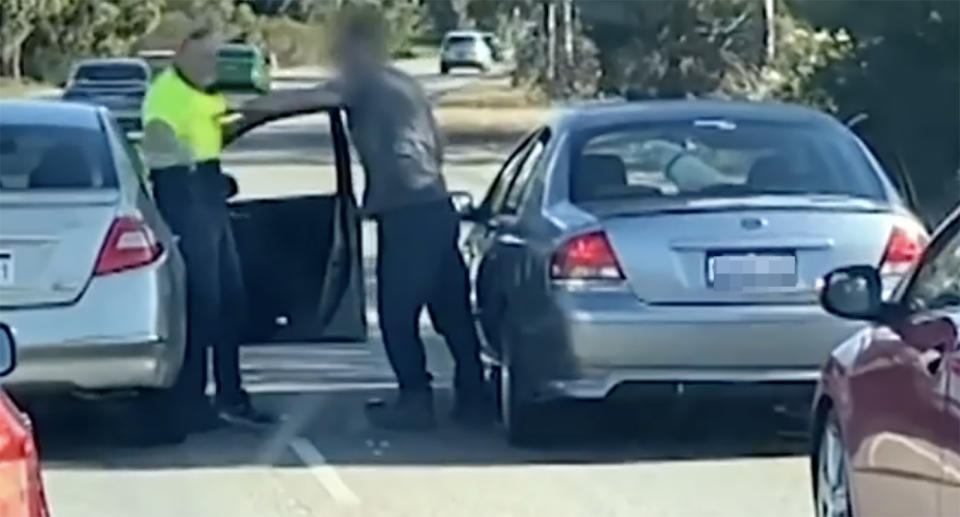 Two men, one next to a Nissan Maxima and the other next to a Ford Falcon, fight on the Tonkin Highway in Perth.