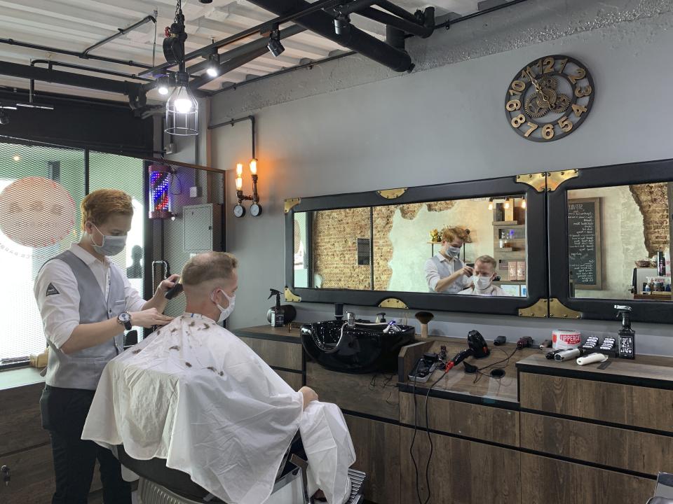 A barber and a male customer wear face masks during a haircut at a barber shop on Tuesday, May 12, 2020 in Singapore. Singapore has allowed selected businesses such as traditional Chinese medicine medical halls, home-based establishments, food manufacturing, selected food retail outlets, laundry services, traditional barbers and pet supplies to reopen May 12 in a cautious rollback of a two-month partial lockdown to curb the spread of COVID-19 infections in the city-state. (AP Photo/Royston Chan)