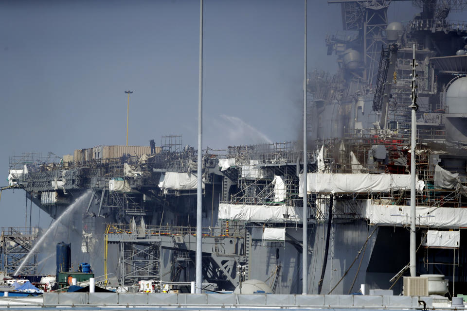 FILE - In this July 12, 2020 file photo fire crews spray water from the dock onto the side of the USS Bonhomme Richard, in San Diego. A sailor accused of starting the fire that destroyed the USS Bonhomme Richard will face a court martial for arson. The Navy notified Ryan Mays on Friday, Feb. 25, 2022, that he was to be tried in military court on two counts for the July 2020 blaze that injured dozens of personnel aboard. (AP Photo/Gregory Bull, File)