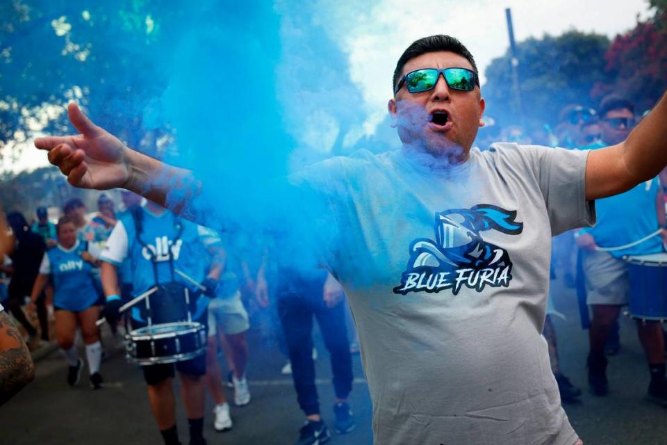 Arturo Vasquez, of Charlotte, N.C., walks through colored smoke while marching with other fans before a game between Charlotte FC and Columbus Crew at Bank of America Stadium in Charlotte, N.C., Saturday, July 30, 2022.