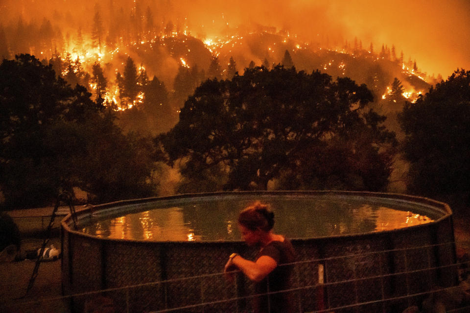 Angela Crawford leans against a fence as a wildfire called the McKinney fire burns a hillside above her home in Klamath National Forest, Calif., on Saturday, July 30, 2022. Crawford and her husband stayed, as other residents evacuated, to defend their home from the fire. / Credit: Noah Berger / AP