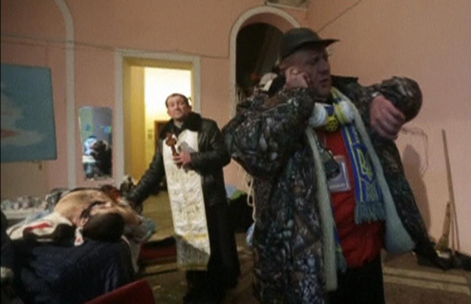 A still image from a video footage shows a priest standing near the body of a man, whom eyewitnesses say was a pro-European protester, inside a makeshift hospital in Kiev