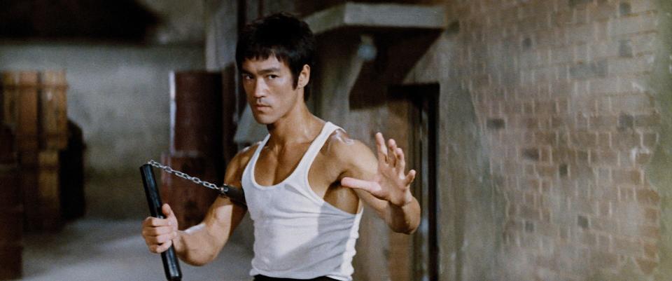 Bruce Lee in a white shirt holding nunchaku