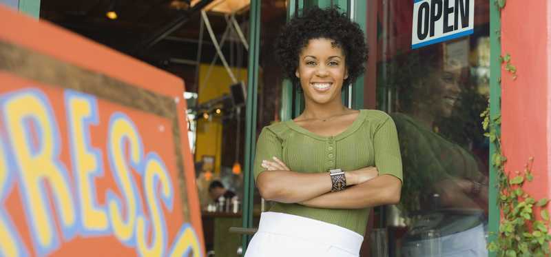 smiling woman wearing apron standing outside coffee shop with her arms folded