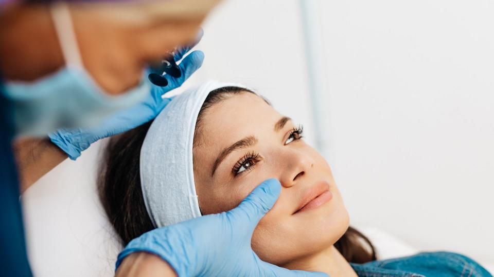 Attractive young woman is getting a rejuvenating facial injections at beauty clinic. The expert beautician is filling female wrinkles by botulinum.