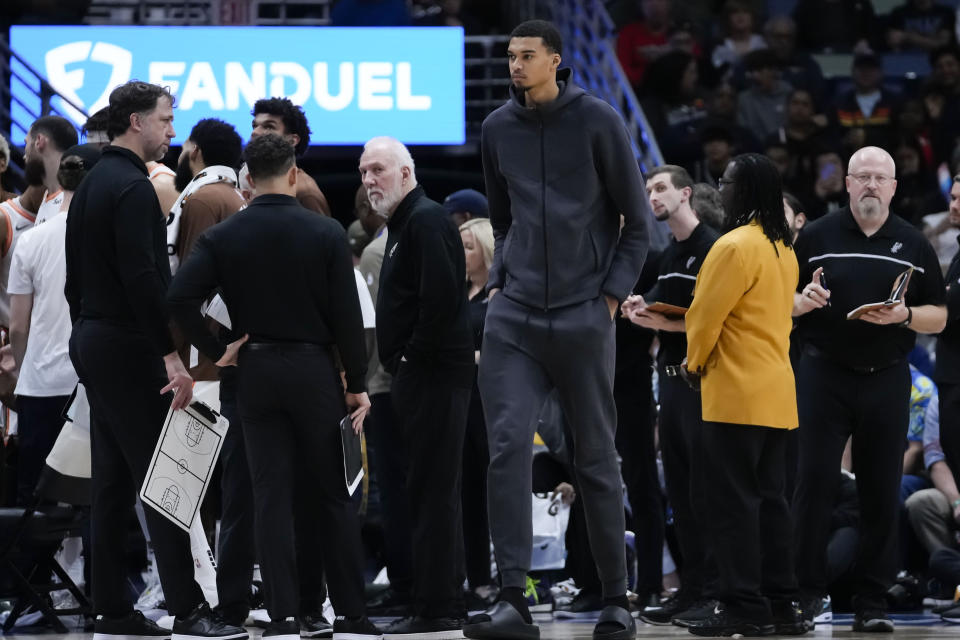 San Antonio Spurs center Victor Wembanyama walks along the bench in street clothes during a timeout in the first half of an NBA basketball game against the New Orleans Pelicans in New Orleans, Friday, Dec. 1, 2023. (AP Photo/Gerald Herbert)